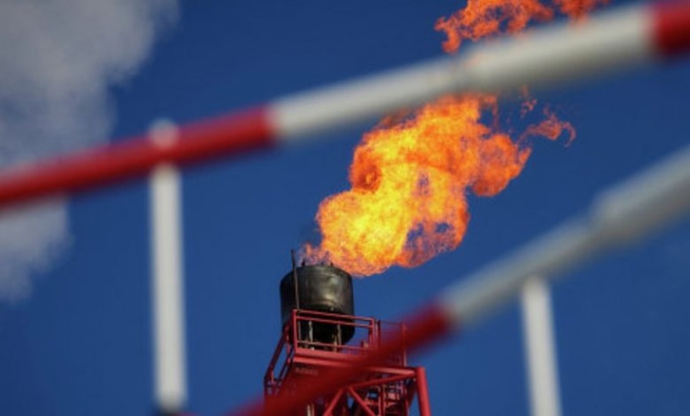 Torchère d'une plateforme pétrolière avec flamme orange sur fond de ciel bleu.