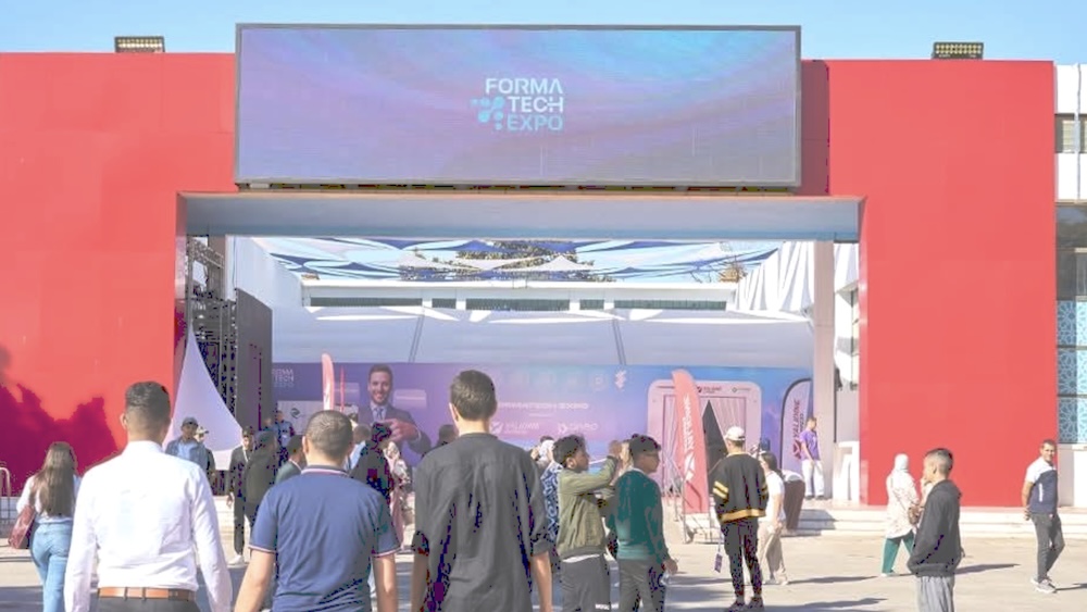 Des visiteurs franchissent le portail d’entrée du salon FormaTech Expo 2025 à la SAFEX d’Alger, un événement consacré à la formation professionnelle et aux métiers du numérique, sous une structure rouge et bleue ornée d’un grand écran.