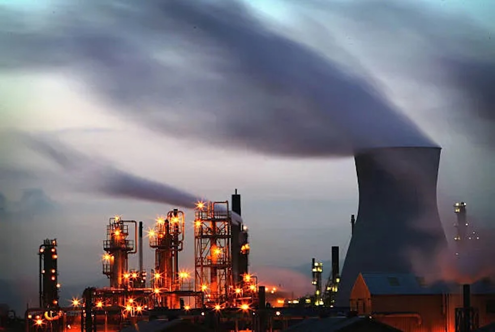 Raffinerie pétrolière éclairée au crépuscule, avec colonnes industrielles et panaches de fumée .