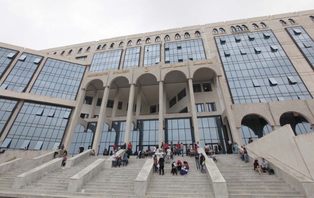 Étudiants assis sur les marches de l'université d'Alger, bâtiment moderne avec façade en verre et arches.